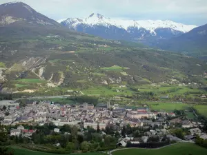 Paysages des Hautes-Alpes - Vallée de la Durance : vue sur les toits de la vieille ville d'Embrun, la rivière Durance bordée d'arbres, les prairies et les montagnes aux cimes enneigées
