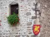 Pérouges - Stone facade with Coat of Arms of Pérouges, window decorated with a geranium and wall lantern