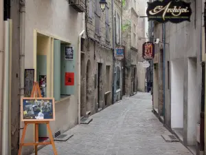 Pézenas - Altstadt: Staffelei, Gasse mit Kopfsteinpflaster gesäumt von Boutiquen und Häusern