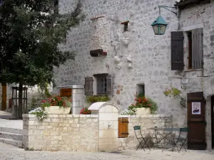 Pujols - Facade of a stone house, tree, flowers, and table with two chairs