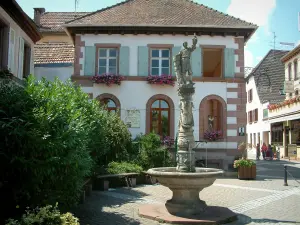 Ribeauvillé - Plaza con una fuente, plantas y casas decoradas con flores (geranios)