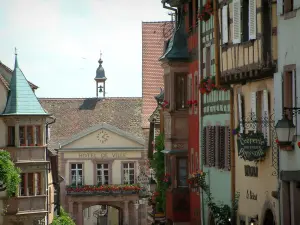 Riquewihr - Houses with colourful facades, oriel windows and forged iron shop signs, building of the town hall in background