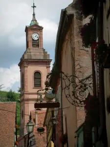 Riquewihr - Houses with colourful facades decorated with forged iron shop signs and the church bell tower in background