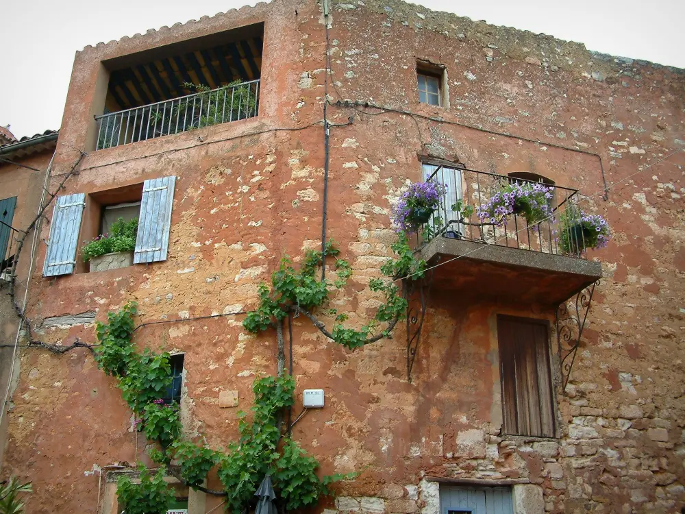 Roussillon - Maison de couleur ocre rouge avec un petit balcon, des plantes et des fleurs