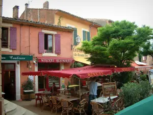 Roussillon - Place avec terrasses de restaurants, parasols et maisons aux façades ocre