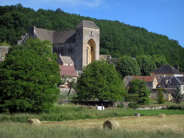 Saint-Amand-de-Coly - Iglesia de la abadía fortificada, casas de pueblo, pacas de heno en un campo y los árboles, en el Périgord negro