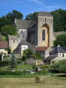 Saint-Amand-de-Coly - Iglesia de la abadía fortificada, casas de pueblo, con balas de paja en un campo y los árboles, en el Périgord negro