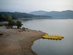 Saint-Cassien lake - Beach, trees, yellow pedal boats moored to a pontoon, lake, shores and hills covered with forests