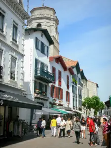 Saint-Jean-de-Luz - Häuserfassaden und Geschäfte (Einkaufsstrasse) der Strasse Gambetta, Glockenturm der Kirche Saint-Jean-Baptiste dominierend die Gesamtheit