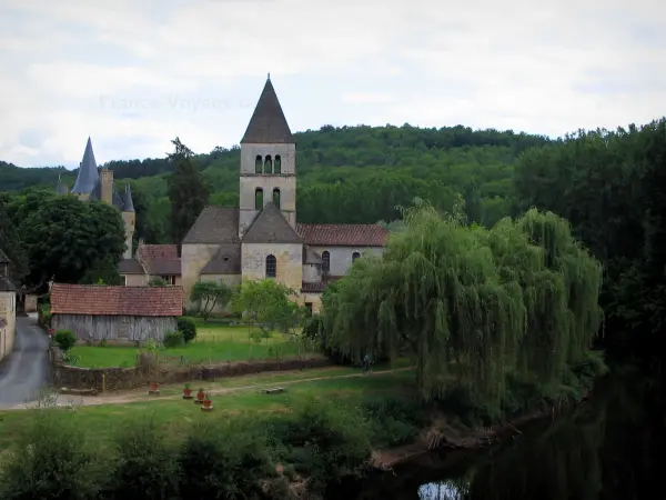 Saint-Léon-sur-Vézère - Romanesque church, Vézère river, bank, weeping willow trees along the water, houses of the village, the Clérans castle and the forest in background, in Périgord