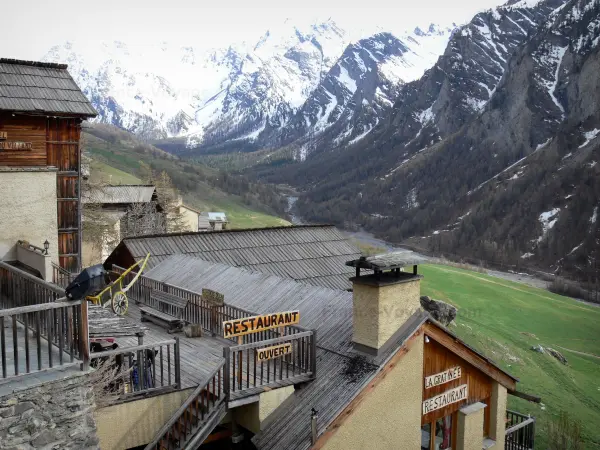Saint-Véran - Roofs of houses of the mountain village covered with larch shingles and view of the torrent and mountains in with snowy tops (snow); in the Queyras Regional Nature Park