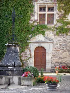 Sainte-Eulalie-d'Olt - Fontana sormontata da una croce, porta e montanti delle finestre una casa di pietra, e le decorazioni floreali del medievale