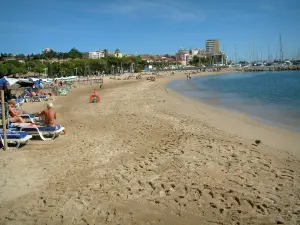 Sainte-Maxime - Zandstrand, parasols en ligbedden met vakantiegangers, Middellandse Zee, zeilboten (boten) van de jachthaven, pijnbomen en palmbomen, huizen en gebouwen van het resort