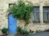 Sainte-Suzanne - Facciata di una casa in pietra con la sua porta blu e ornamenti floreali