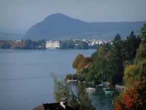 See von Annecy - Bäume mit Herbstfarben, Häuser am Rande des Sees, Bauten der Stadt Annecy und Hügel im Hintergrund