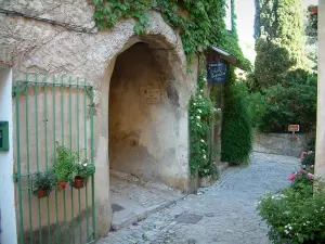 Séguret - Geplaveide straat met een boog en een huis versierd met rozen, planten en bloemen