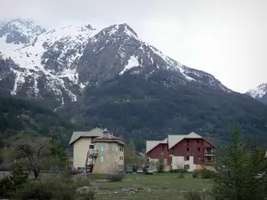 Serre-Chevalier - Serre-Chevalier 1500 (Le Monêtier-les-Bains), Ski-Station (Wintersportort): Häuser, Wiese, Bäume und Berg mit schneebedecktem Gipfel (Schnee); im Nationalpark Écrins