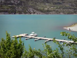 Serre-Ponçon lake - Branches of trees in foreground, water reservoir (artificial lake), pontoon of the water sports centre of Savines-le-Lac and shores