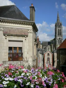 Sillé-le-Guillaume - Flores en el primer plano con una vista de la torre del campanario de Notre Dame y las fachadas de las casas de la ciudad