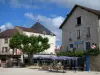 Souillac - Terrasses de cafés, arbre, maisons de la ville et nuages dans le ciel bleu