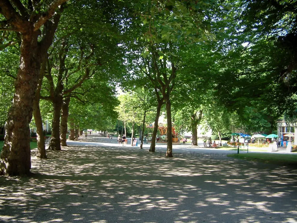 Les stations thermales des Vosges - Vittel: Allée ombragée du parc thermal avec arbres, carrousel et terrasse de café