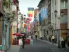 Strasbourg - Grand'Rue avec drapeaux suspendus, maisons décorées de fleurs, terrasse de café et boutiques