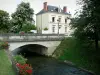 Tal des Loir - Flussbrücke überspannend den Fluss Loir, Hausfassade, Blumendekorationen und Bäume am Wasserrand; in La Chartre-sur-le-Loir