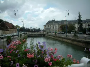 Troyes - Rambarde d'un pont décorée de fleurs avec vue sur le cours d'eau, les lampadaires et les bâtiments de la ville