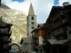 Val-d'Isère - Romanische Kirche und Chalets des Dorfes (Wintersportort), Berg und Wolken im Himmel (peripherische Zone des Nationalparks Vanoise)