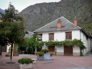 Valbonnais - Village of Entraigues: square with fountain, trees and flowers, houses of the village and mountains in the background