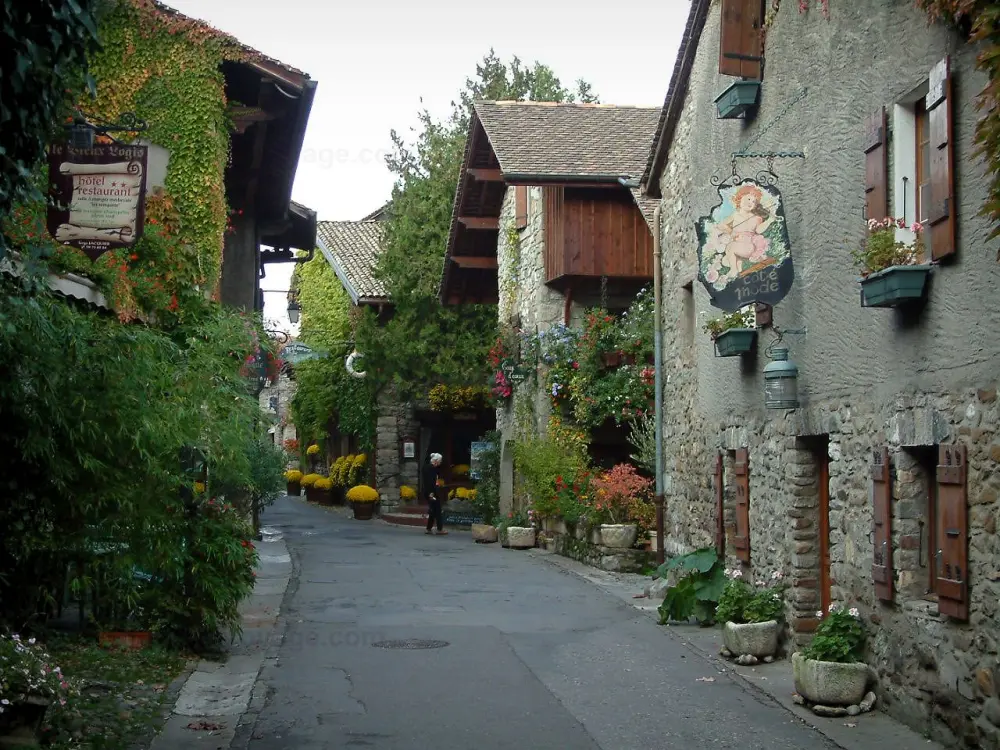 Yvoire - Rue fleurie du village médiéval avec maisons aux façades ornées d'enseignes, pots de fleurs et plantes grimpantes