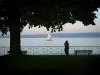 日内瓦湖 - 树，夫妇，长凳和栏杆在阴影俯视日内瓦湖，风船和瑞士岸在背景中