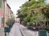 Aigues-Mortes - Strasse, Bäume, Restaurant-Terrasse und Häuserfassaden, hinter den Stadtmauern