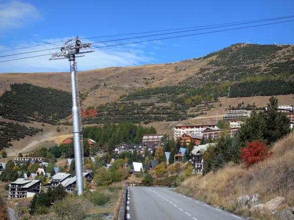 Alpe d'Huez - Estrada, teleférico, chalés e edifícios da estância de esqui de inverno e verão (estação de esqui) no outono, montanha pontilhada com árvores e pastagens