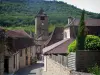 Autoire - Rue bordée de maisons, clocher de l'église et arbres, en Quercy