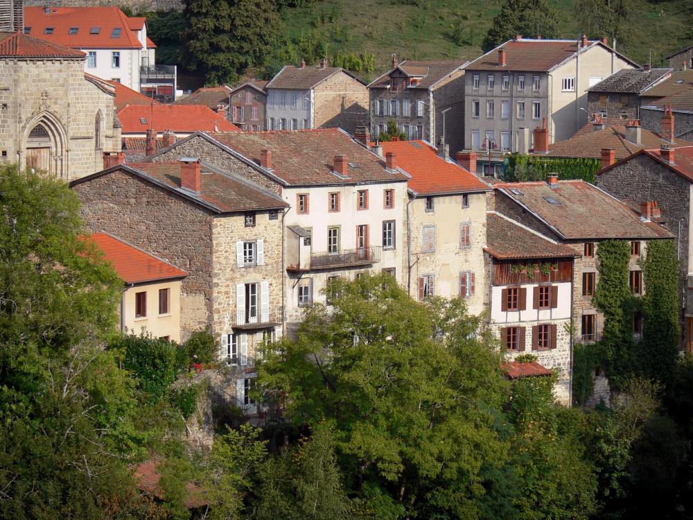 Guide d'Auvergne-Rhône-Alpes - Olliergues - Portail de l'église Notre-Dame, maisons du village et arbres ; dans le Parc Naturel Régional Livradois-Forez