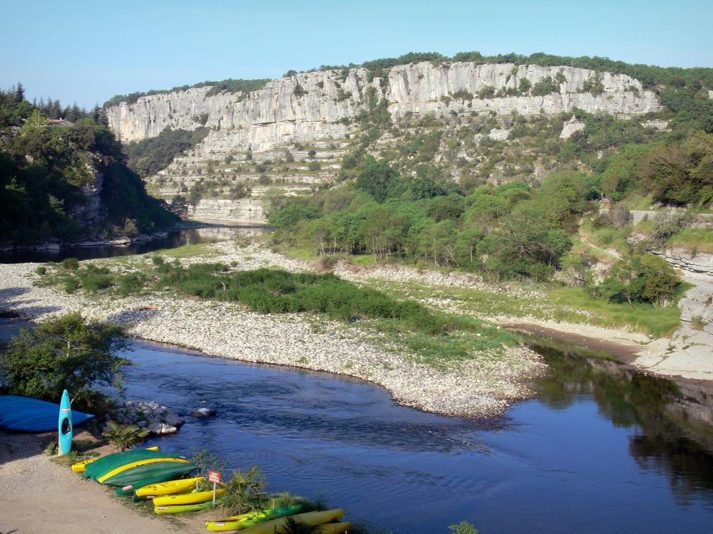 Guide d'Auvergne-Rhône-Alpes - Paysages de l'Ardèche - Vallée de l'Ardèche, à Balazuc : canoës posés le long de la rivière Ardèche ; falaises dominant l'ensemble
