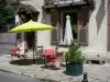 Barbizon - Hausfassade und Gehsteig geschmückt mit einer Pflanztröge, Tischen, Stühlen und einem Sonnenschirm