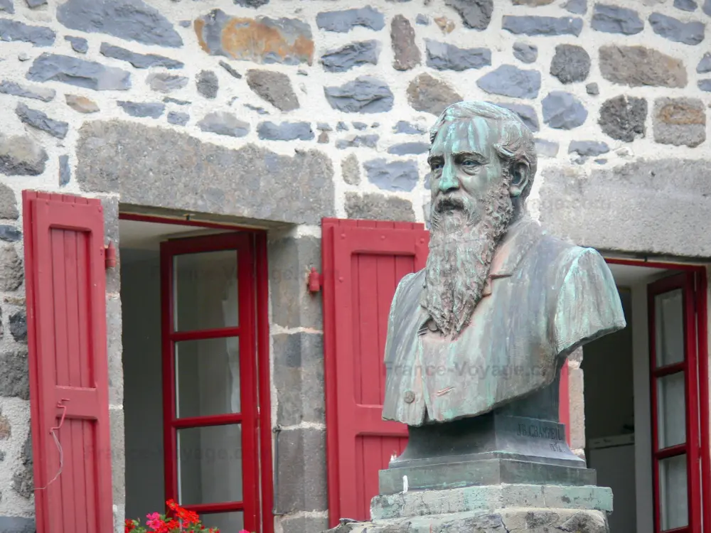 Guía de Cantal - Salers - Busto de Pierre-Ernest Tyssandier Escous y la fachada de una casa de piedra con persianas de color rojo