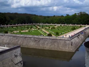 Castelo de Chenonceau - Jardim de Diane de Poitiers com seu jato de água, seus arbustos e seus parterres franceses, fosso, árvores e nuvens no céu