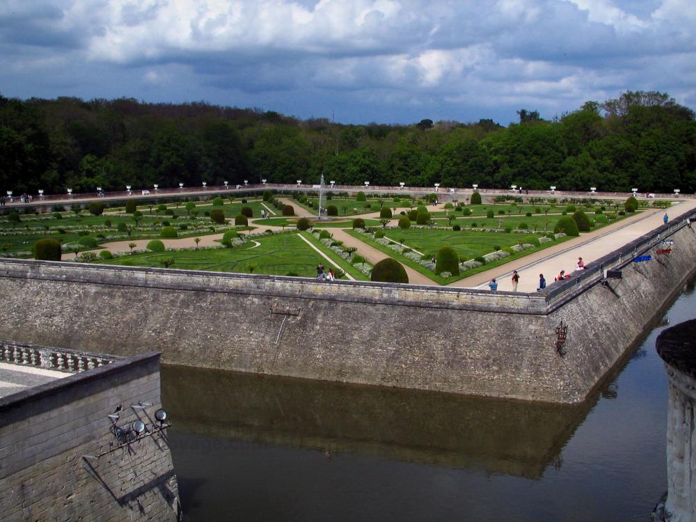 Guide du Centre-Val de Loire - Château de Chenonceau - Jardin de Diane de Poitiers avec son jet d'eau, ses arbustes et ses parterres à la française, douves, arbres et nuages dans le ciel