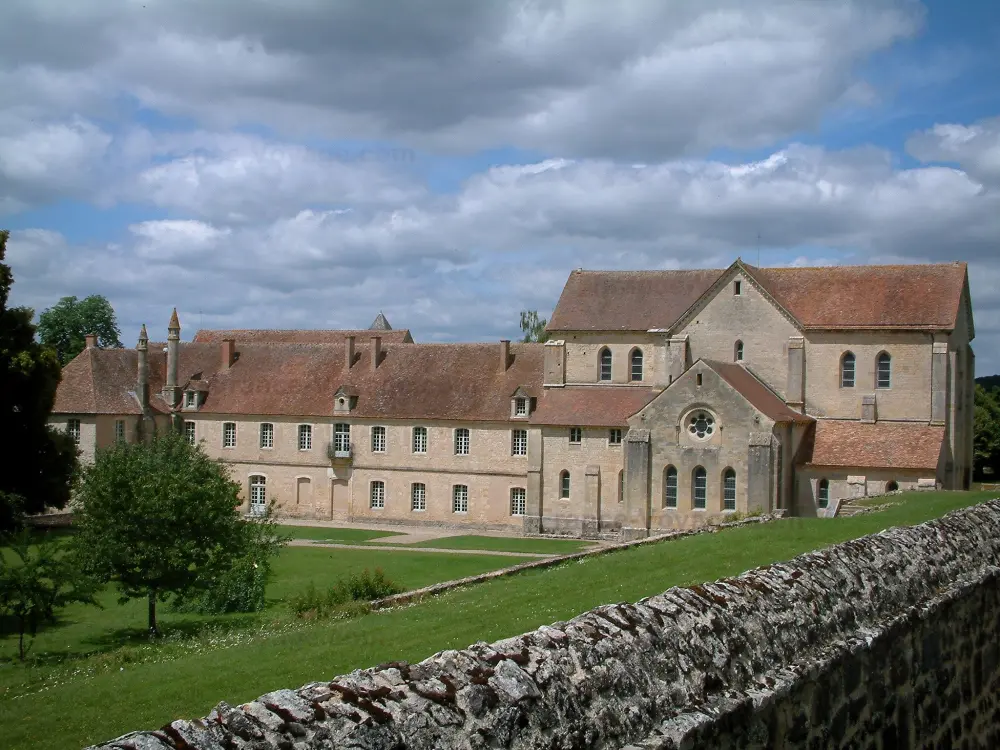 Guía de Cher - Abadía de Noirlac - Abadía cisterciense y un parque con árboles, nubes en el cielo