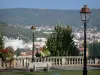 Clermont Ferrand - Praça com um banco, postes de iluminação e flores com vista para as árvores e edifícios da cidade