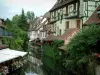 Colmar - La Petite Venise : rivière (la Lauch) avec maisons à colombages aux façades colorées, arbres et terrasse de café