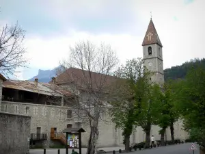 Colmars - Espadaña de la iglesia de Saint-Martin, las paredes y la carretera bordeada de árboles