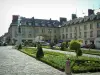Compiègne - Place de l'Hotel de Ville met bloembedden, schoongemaakt struiken en beeld, gebouwen en winkels op de achtergrond