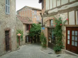 Cordes-sur-Ciel - Rua inclinada pavimentada da cidade medieval, subindo rosas (rosas) e abriga algumas com enxaimel