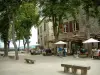 Cordes-sur-Ciel - Vierkante flens met zijn stenen bankjes, bomen, een restaurant met terras, de stenen huizen en uitzicht over de omliggende heuvels