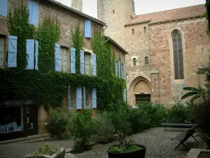 Cordes-sur-Ciel - Praça decorada com bancos e arbustos, casa de pedra coberta de hera com venezianas azuis e igreja Saint-Michel