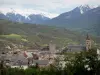 Embrun - Clocher de la cathédrale Notre-Dame-du-Réal, tour Brune (ancien donjon des archevêques) et maisons de la vieille ville avec vue sur les collines couvertes d'arbres et les montagnes aux cimes enneigées ; dans la vallée de la Durance